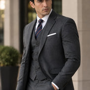 Homem elegante usando terno social cinza three-piece com gravata listrada azul-marinho e vermelha.